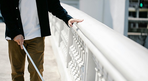 Person mit Blindenstock auf einer Brücke