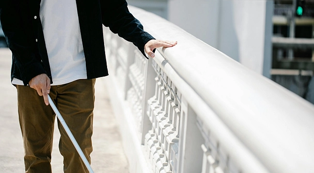 Person mit Blindenstock auf einer Brücke