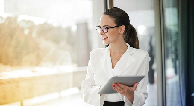 Eine Frau mit Tablet schaut aus dem Fenster