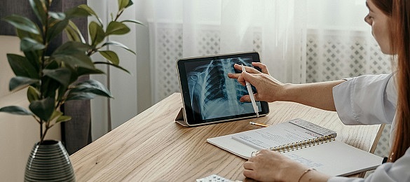 Eine Frau sitzt vor einem Tablet mit Röntgenbild