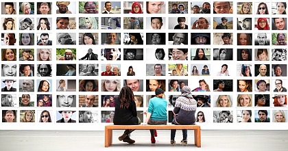 Das Bild zeigt viele kleine Bilder von unterschiedlichen Menschen. Davor sitzen drei Menschen auf einer Bank und schauen sich die Bilder an.
